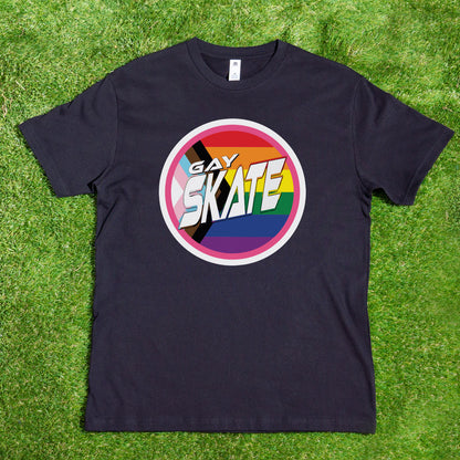 A black "Gay Skate Original Logo - Local hand printed t-shirt" from My Store is laid flat on green grass, showcasing a multicolored circular logo with the text "GAY SKATE" in bold, stylized letters. The background of the logo features a rainbow gradient and a skater silhouette, celebrating the gay skate community.