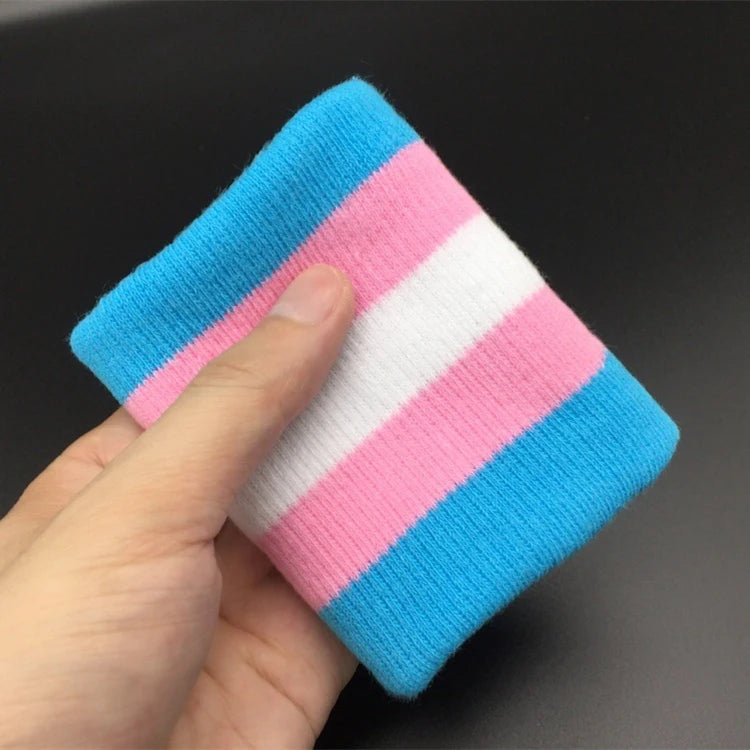 A wrist adorned with the Gay Skate Trans pride flag sporty wrist band featuring horizontal stripes in light blue, pink, and white - the transgender pride flag. An accessory for clubbing, raves, parties and festivals. Perfect for transmen, transgirls, transwomen, non-binary and other genderqueer people.