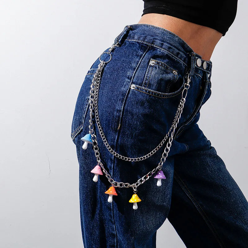 Close-up of a person wearing blue denim jeans adorned with rainbowLayered Rainbow Clip-on Chains - cute kawaii colourful designs, adding a playful harajuku element to the outfit. The chains, consisting of various colors and shapes like hearts and flowers, bring colourful cuteness. The background shows a park with green grass and trees. Acessories include carabiners, mushrooms, safety pins, gummi bears and more for punks, emos, skaters and queer fashionistas.