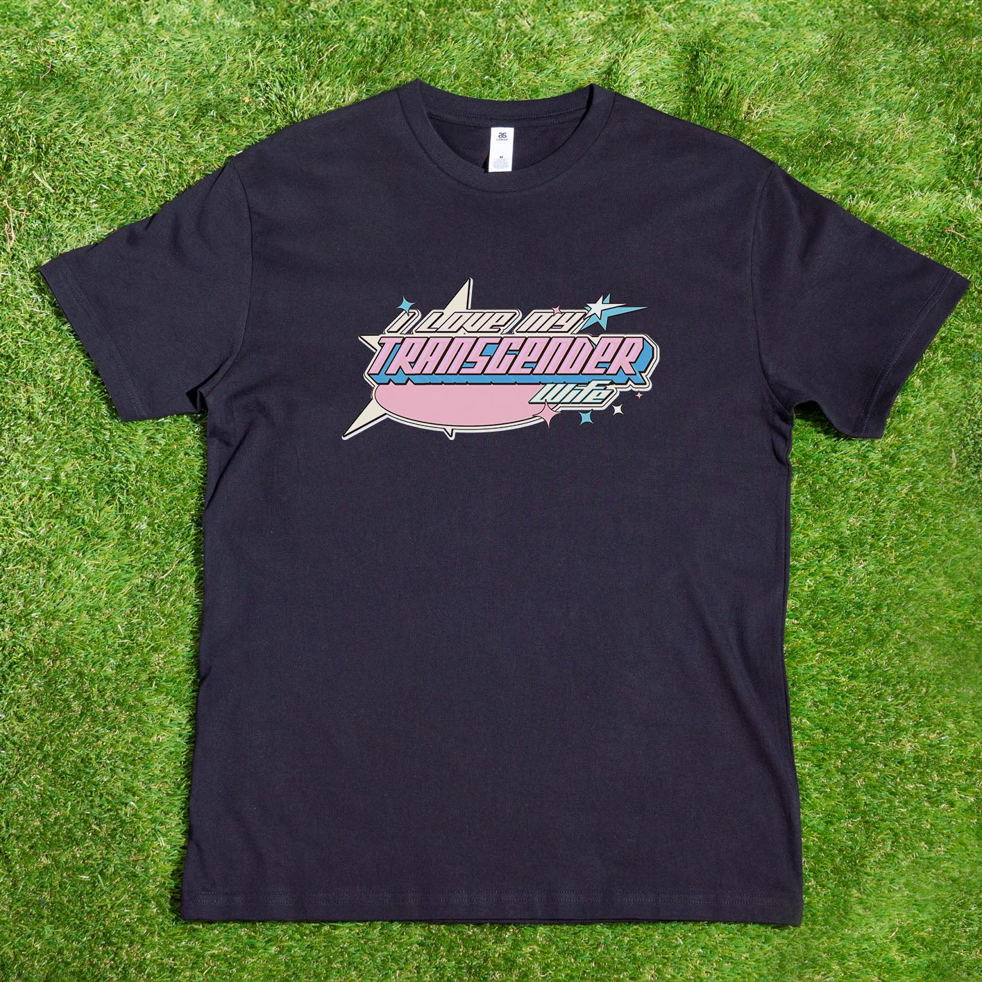 Introducing the "I LOVE MY TRANSGENDER GIRLFRIEND - Local hand printed t-shirt" by Gay Skate. This black T-shirt features an original design with a colorful graphic, where the text "I Love My Transgender Girlfriend" appears in vibrant pink, blue, and white hues. The design is set against a splash-like background with star accents, making it the perfect Pride clothing for those who want to celebrate Transgender Pride in style.