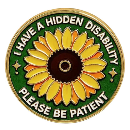 A circular enamel pin featuring a yellow sunflower on a green background with the text 'I HAVE A HIDDEN DISABILITY PLEASE BE PATIENT' in white. The pin is styled on a warm cream surface with beige satin ribbon and small white baby's breath flowers.
