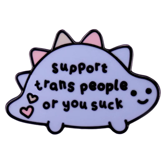 The Gay Skate "Support Trans People or You Suck" dinosaur badge showcases a vibrant cartoon dino with colorful spikes and hearts, playfully supporting the transgender community.