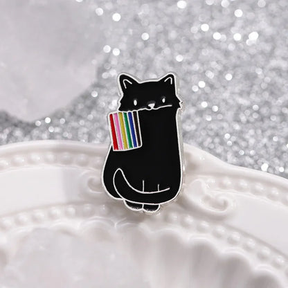 Black cat enamel pin holding a rainbow flag on a textured surface with a glittery background