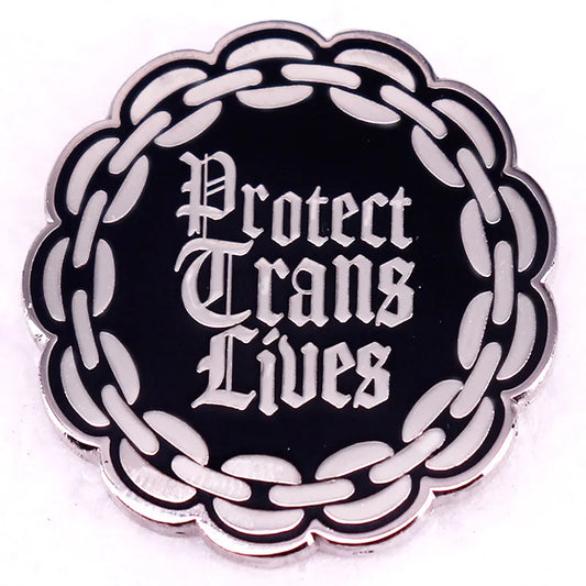 The Protect Trans Lives enamel pin by Gay Skate features bold Gothic-style lettering with a black badge and a white chain border.