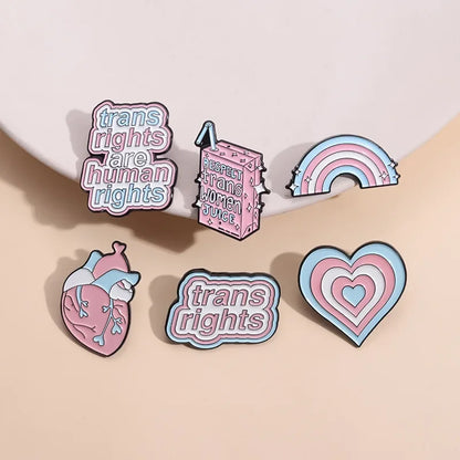 Product Description: The "Trans Rights and Trans Pride" enamel pins collection by Gay Skate includes six beautifully designed badges celebrating transgender pride. Top row designs feature: "Trans Rights Are Human Rights," "Trans Rights," and "Respect Trans Women Juice." Bottom row designs include an anatomical heart with trans flag colors, a heart with layered trans flag colors, and a rainbow with trans flag colors.