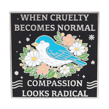 A square enamel pin with a black background and silver border, featuring a blue bird perched on white and peach flowers with the text 'WHEN CRUELTY BECOMES NORMAL' and 'COMPASSION LOOKS RADICAL'.