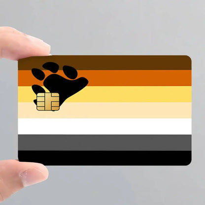 A hand holding a rectangular card featuring the bear pride flag colors with a black bear paw and gold chip
