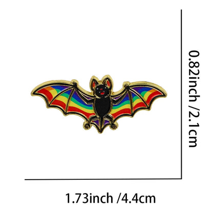 A bat-shaped enamel pin with rainbow wings and a black body outlined in gold