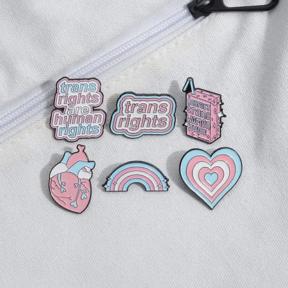 Product Description: The "Trans Rights and Trans Pride" enamel pins collection by Gay Skate includes six beautifully designed badges celebrating transgender pride. Top row designs feature: "Trans Rights Are Human Rights," "Trans Rights," and "Respect Trans Women Juice." Bottom row designs include an anatomical heart with trans flag colors, a heart with layered trans flag colors, and a rainbow with trans flag colors.