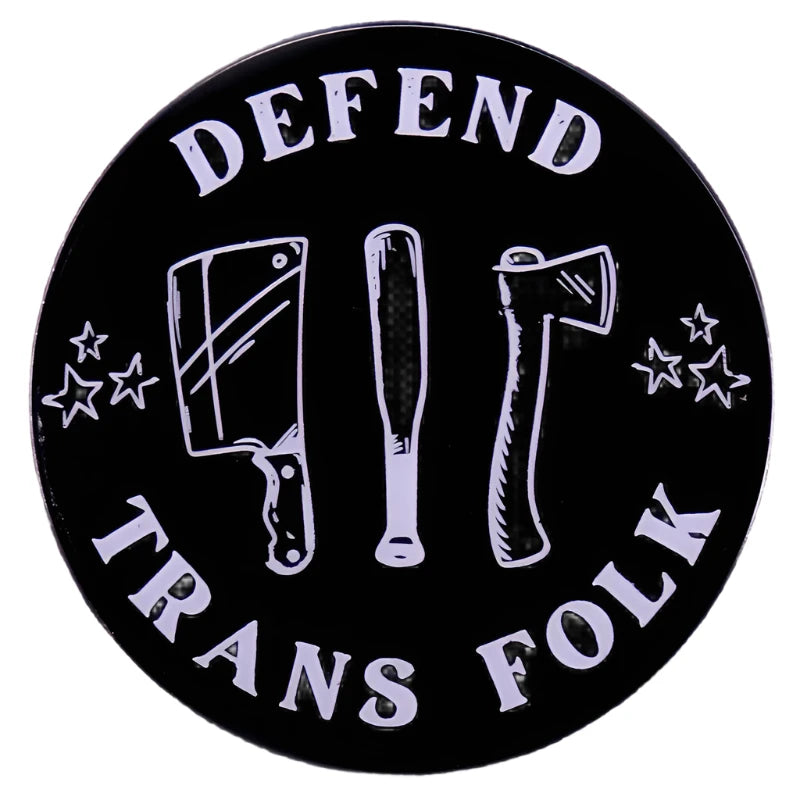 The Defend Trans Folk Enamel Pin by Gay Skate features the phrase "Defend Trans Folk" in white on a round badge, with a cleaver, bat, and axe surrounded by stars on a black background—a striking symbol confronting transphobia.