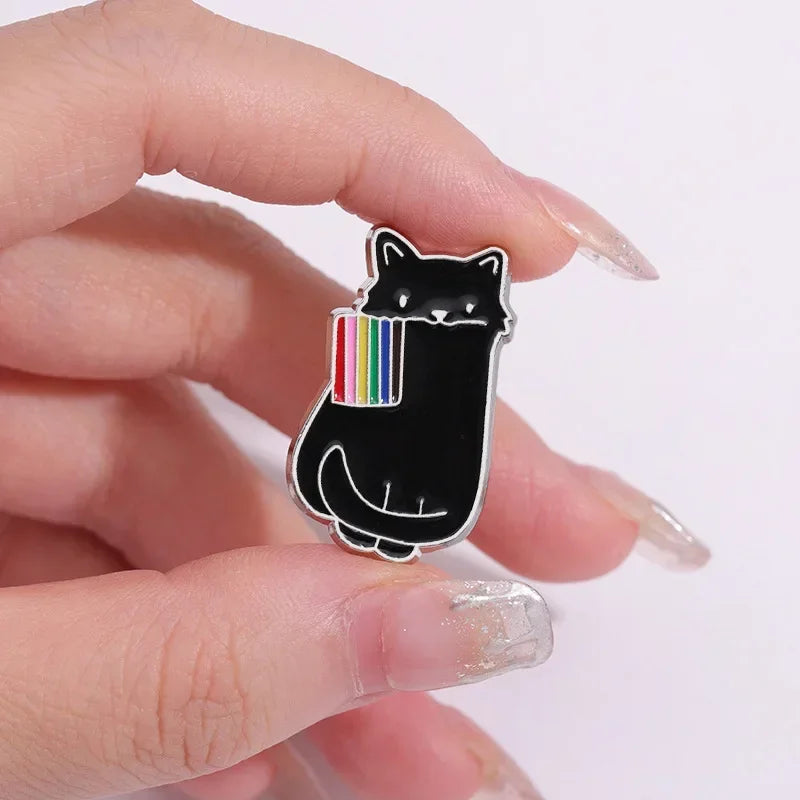 Black cat-shaped pin with rainbow design held between fingers on a white background