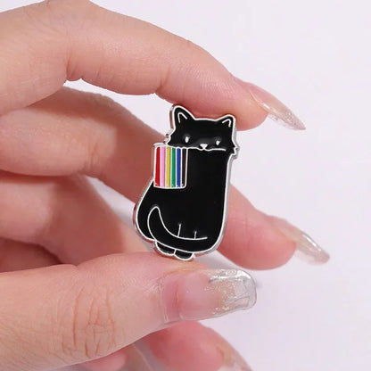 Black cat-shaped pin with rainbow design held between fingers on a white background