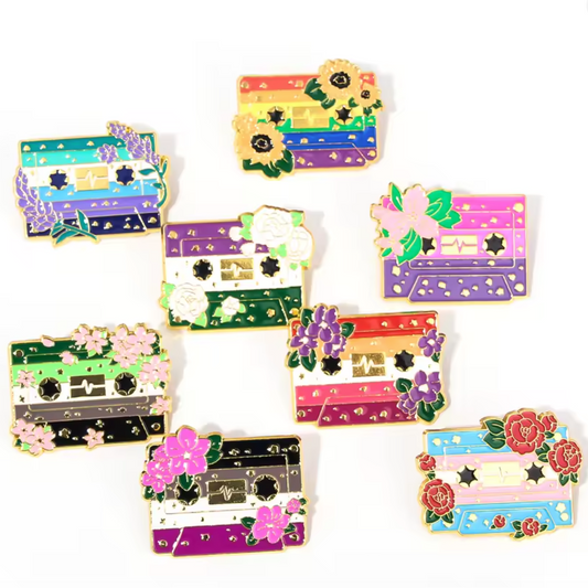 Colorful pride flag badges as cassette tape-shaped pins with floral decorative elements 