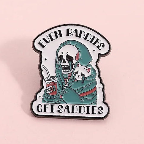 Enamel pin with a skeleton holding a cat and text 'Even Baddies Get Saddies' 