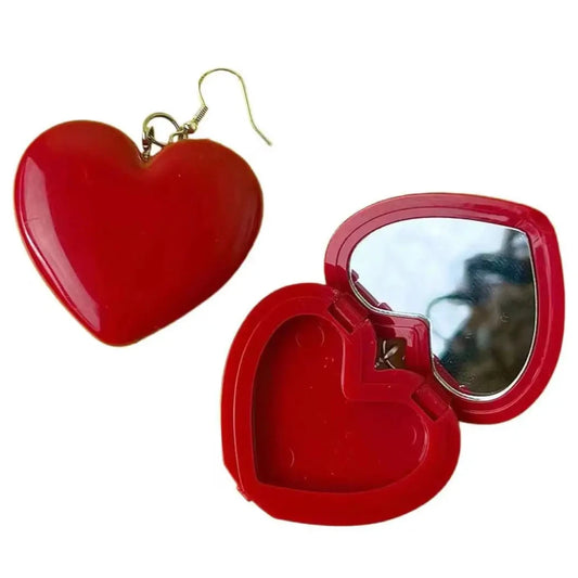 A red Y2K Heart Mirror Earring with a hook is placed next to an open compact mirror. The heart-shaped mirror case, by the brand Gay Skate, is also red, perfectly complementing the earring's charming design.