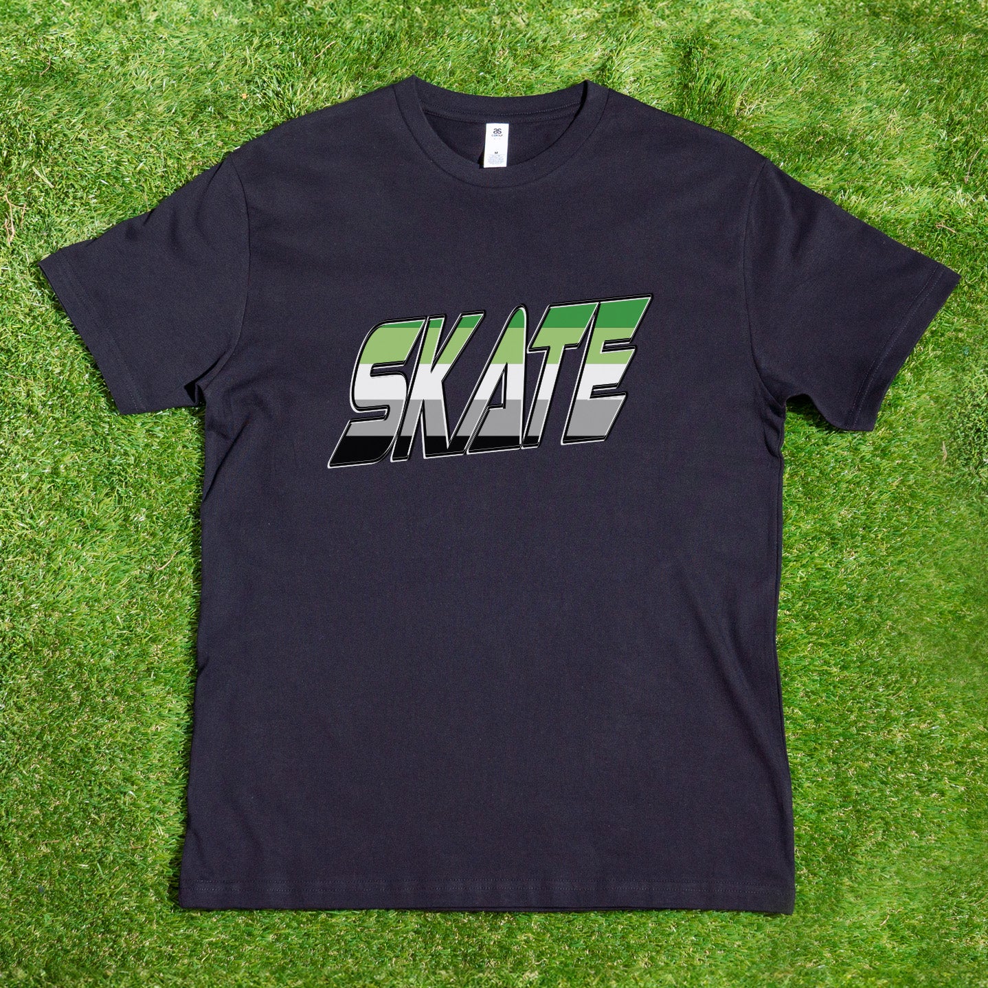 The "SKATE Aromantic Pride" T-shirt by Gay Skate, featuring bold and stylized green white and gray and black Aro flag lettering on a black AS Colour shirt, is perfect for GAY SKATE events or casual outings. Presented against a backdrop of lush green grass, this trendy top stands out with its local hand-printed design.