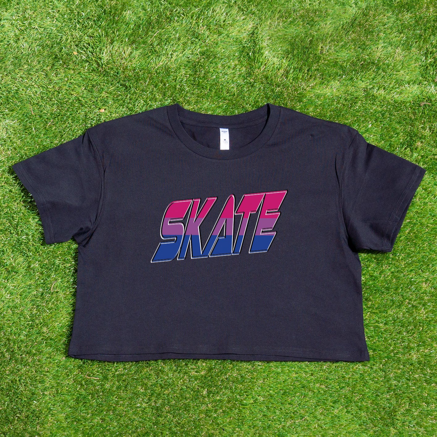 The "SKATE bisexual pride flag - locally printed crop tee" by Gay Skate is a black cropped T-shirt featuring the word "SKATE" printed across the front in a bold, gradient design that transitions from red at the top to pink, purple, and blue at the bottom. Perfect for Queer Skate events, it showcases text with a slightly 3D effect and a retro, angular font style.