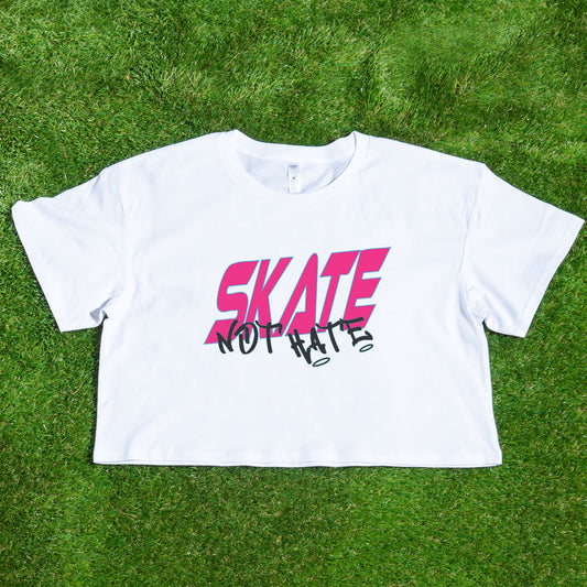 The SKATE NOT HATE original logo crop tee by Gay Skate is a white, short-sleeved shirt featuring the word "SKATE" in bold, pink, slanted capital letters across the chest. The message is accentuated with the word "NOT" in black, distorted text overlaying "SKATE," promoting the message: skate not hate.