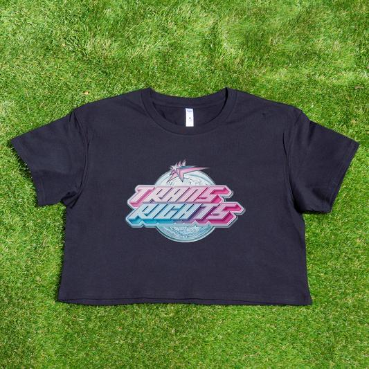 Against a vibrant green grass background, this black crop tee, named the "TRANS RIGHTS new design - locally printed crop tee," showcases a colorful retro motif with bold gradient lettering spelling out "TRANS RIGHTS." Celebrate pride with this distinctive piece from Gay Skate, a trans-owned brand that perfectly complements the queer skate streetwear scene.