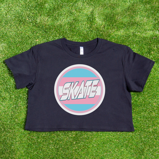 The SKATE Trans Flag round logo - locally printed crop tee by Gay Skate is a black cropped shirt that showcases a round emblem in the center, featuring the word "SKATE" in white stylized text. The emblem is bordered in blue and pink stripes, reminiscent of the trans flag logo, making it a standout piece of queer skatewear.