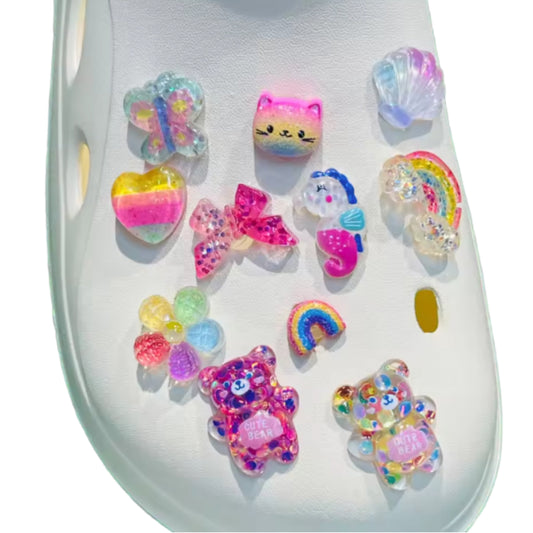 Close-up of a white clog decorated with the Acrylic Rainbow Shoe Charms set of 10, including colorful designs like a butterfly, cat, shell, heart, bows, seahorse, rainbows, flower, and two cheerful teddy bears.