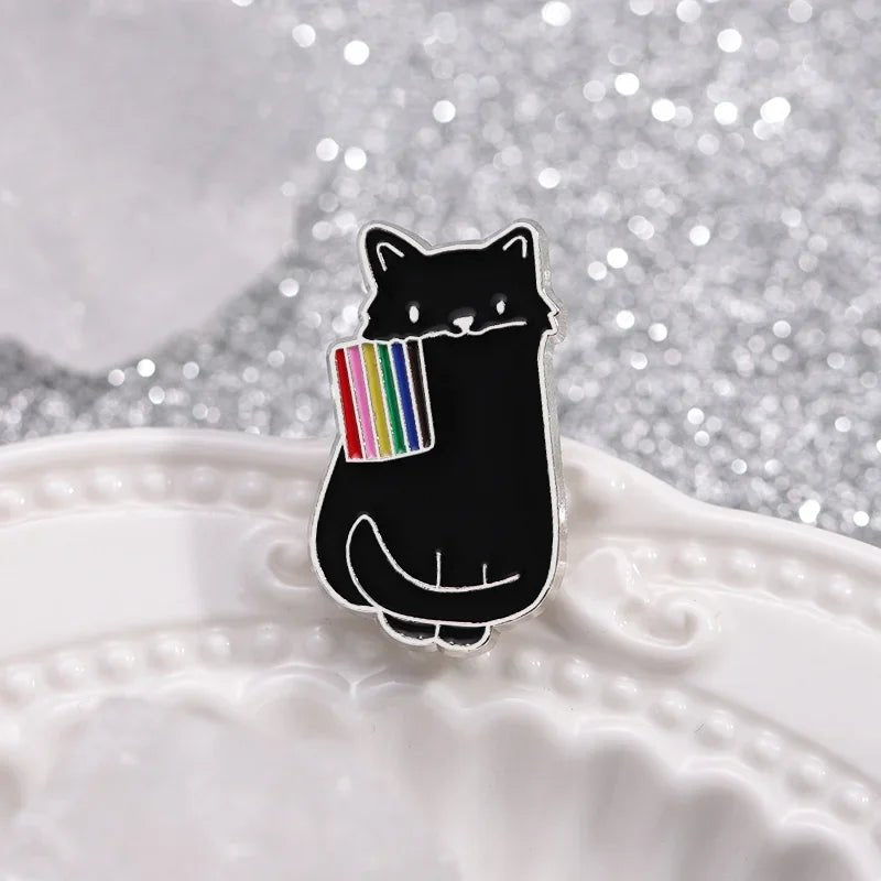 Black cat enamel pin holding a rainbow flag on a textured surface with a glittery background