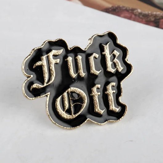 A black enamel lapel pin with gold trim and raised gothic lettering that reads 'Fuck Off'