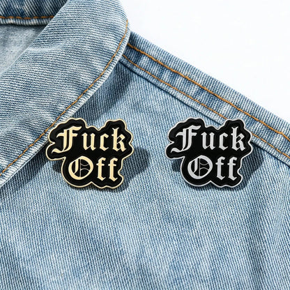 Two black enamel lapel pins with the text 'Fuck Off' in a gothic font, displayed on a light blue denim jacket.