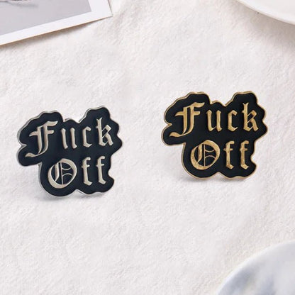 Two enamel lapel pins with the phrase 'Fuck Off' in a gothic font, one in black with gold lettering and outline, and the other in black with silver lettering and outline