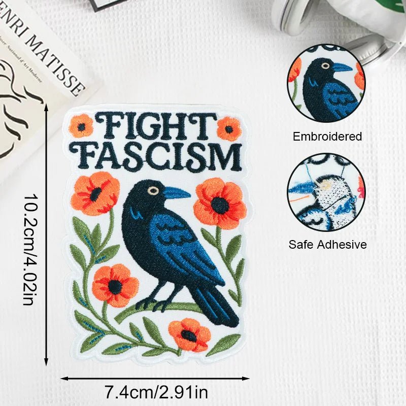 Embroidered patch with a crow and flowers and text 'Fight Fascism' on a white background.