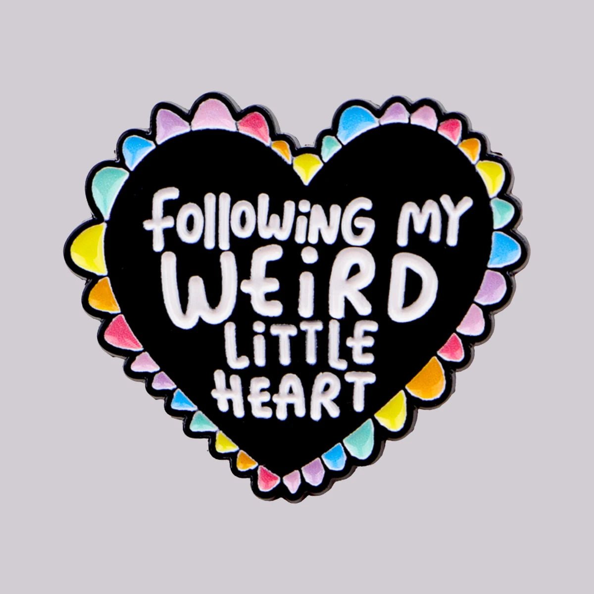 The "Following My Weird Little Heart - enamel pin" features a black and rainbow heart with a colorful border and bold, playful white text—an ideal pride accessory for adding personality to your collection.