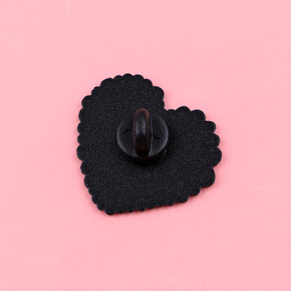 The Following My Weird Little Heart enamel pin features a black and rainbow heart with a scalloped edge and looped fastener, displayed on a solid pink background—perfect as a pride accessory.