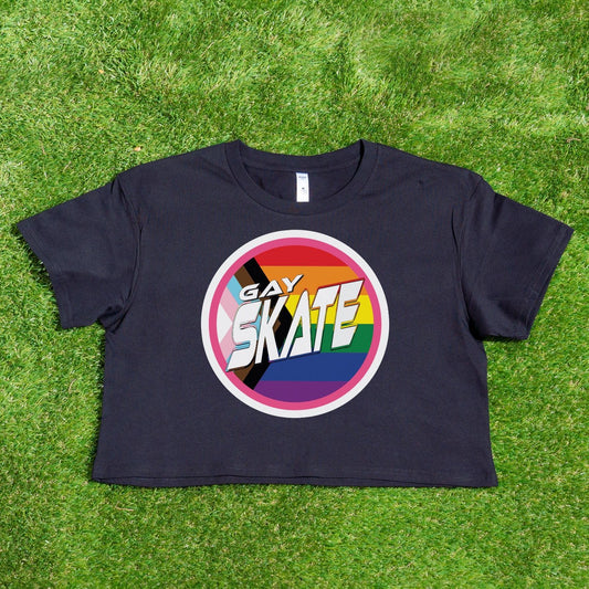 A vibrant "GAY SKATE original logo - locally printed crop tee" from Gay Skate, featuring a circular logo with the text “Gay Skates” on a rainbow background symbolizing LGBTQ+ pride, lies flat on a grassy surface. This queer skate-inspired cropped pink T-shirt exudes inclusivity and energetic spirit.