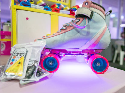 A pastel-colored roller skate with pink Hebegb wheels is illuminated by Gay Skate's vibrant  rechargeable LED skate lights. The skate lights, from the brand Gay Skate are displayed on a table beside the product which includes a small remote control, charger, and other roller skate accessories. This product is available with Australian shipping and International shipping.