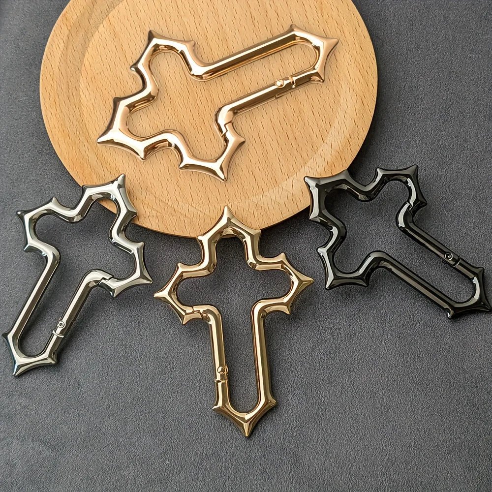 Gold, silver and black Gothic cross carabiners displayed on a grey surface and round wooden board.
