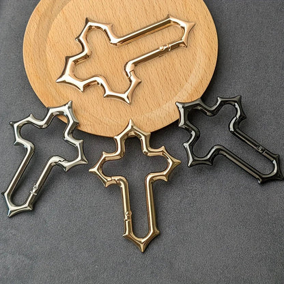 Gold, silver and black Gothic cross carabiners displayed on a grey surface and round wooden board.