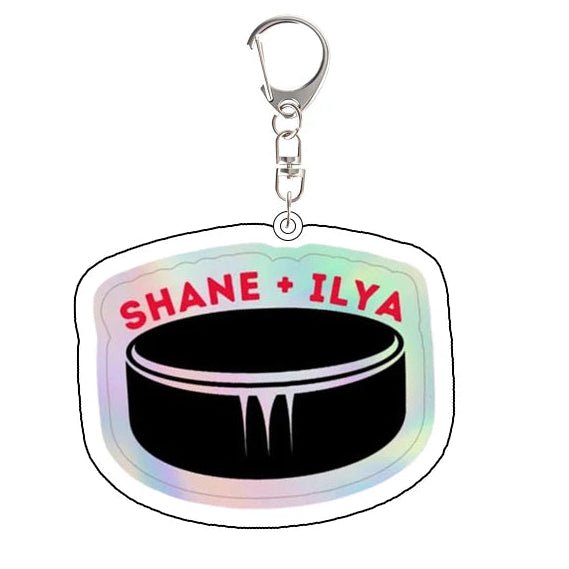 Heated Rivalry Keychain with hockey puck design and 'Shane + Ilya' text 