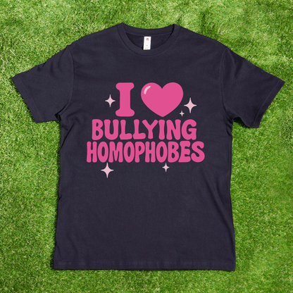 A black AS Colour tee reading "I 🩷 Bullying Transphobes / Homophobes" in pink is shown on grass, surrounded by sparkles—hand printed by a trans-owned business specializing in queer streetwear.