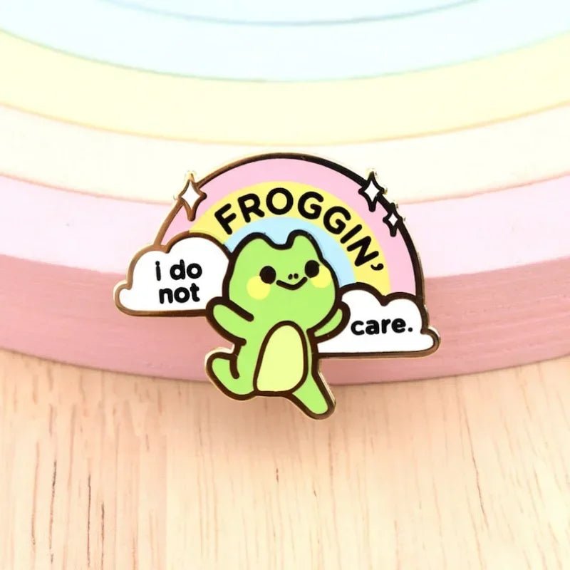 I Do Not Froggin' Care rainbow enamel pin. Cartoon frog character with rainbow and cloud text on a pastel background