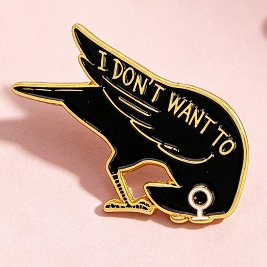 A black and gold enamel pin shaped like a crow with the text 'I DON'T WANT TO' 
