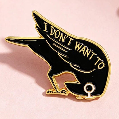 A black and gold enamel pin shaped like a crow with the text 'I DON'T WANT TO' 