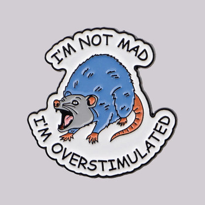Enamel pin with a cartoon possum and text 'I'm not mad, I'm overstimulated' 