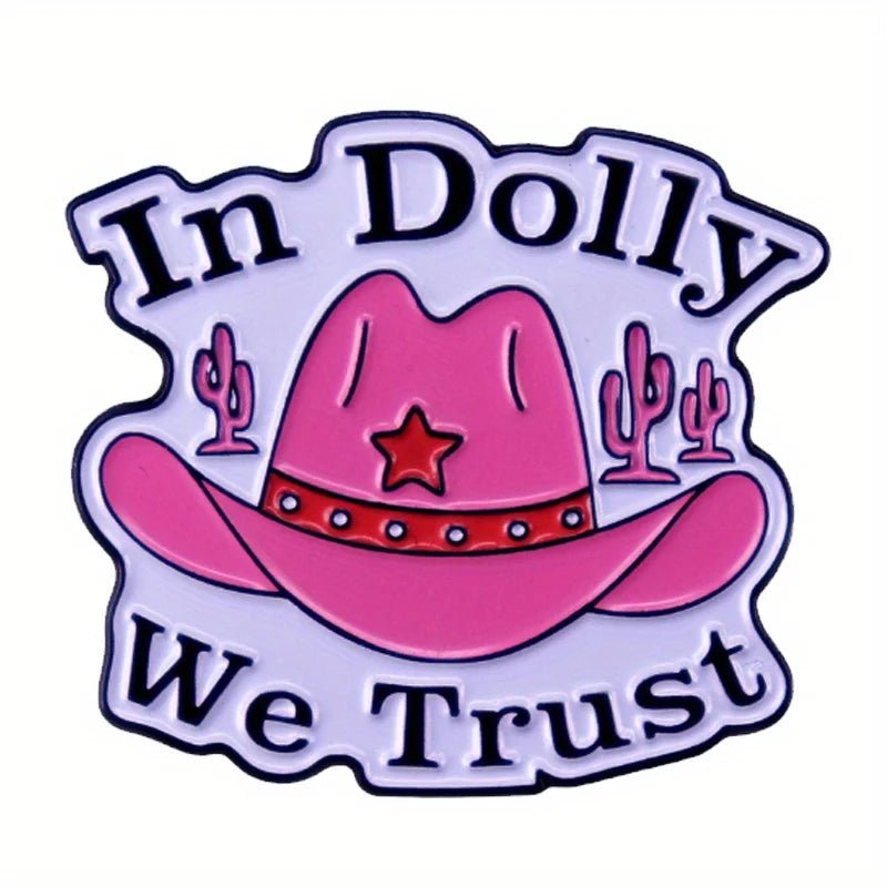 A pink cowgirl hat enamel pin called “In Dolly We Trust,” featuring a red star, cacti in the background, and the phrase “In Dolly We Trust” surrounding the hat.