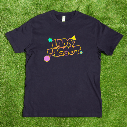 A black Lady F@gg*t - Local hand printed t-shirt lays on grass, showcasing the phrase in bold, colorful letters surrounded by stars, a circle, and geometric shapes.