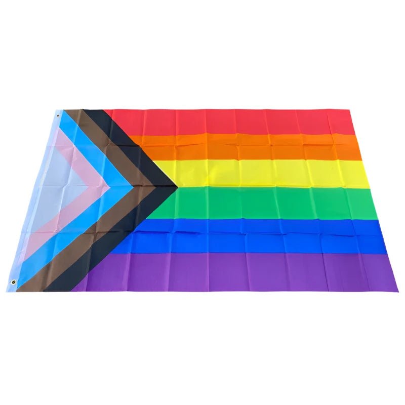 This image showcases the 150cm x 90cm Progress Pride Rainbow Flag by Gay Skate. It is made of high-quality polyester and features traditional rainbow stripes, along with a chevron on the left that includes black and brown stripes, plus light blue, white, and pink stripes to represent marginalized LGBTQ+ communities, including people of color and the trans community.