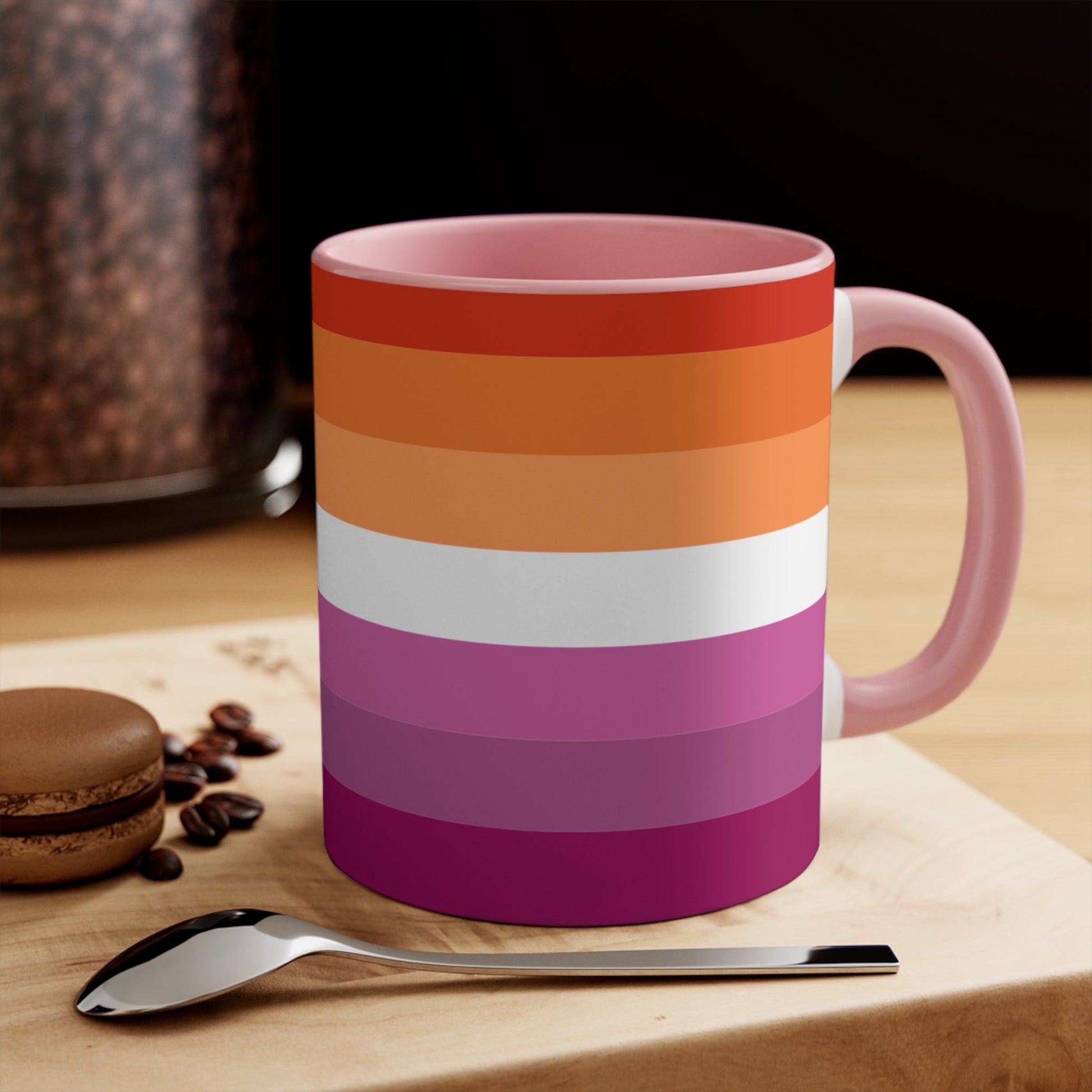 The Lesbian pride flag colorful accent mug by Printify features a vibrant design with horizontal stripes in varying shades of orange, pink, and purple. It has a red handle and colorful interior that create an eye-catching contrast against the plain white background.