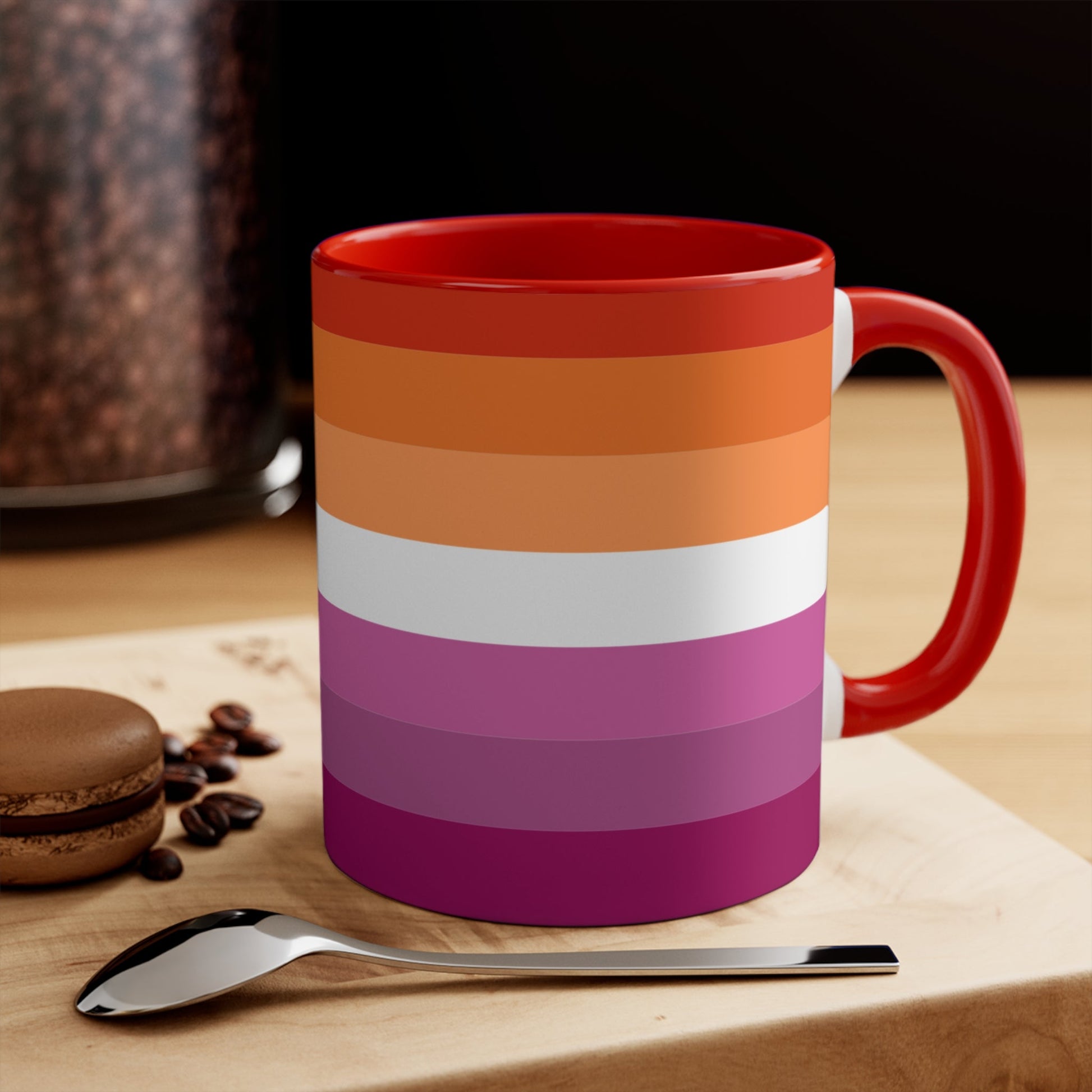 The Lesbian pride flag colorful accent mug by Printify features a vibrant design with horizontal stripes in varying shades of orange, pink, and purple. It has a red handle and colorful interior that create an eye-catching contrast against the plain white background.