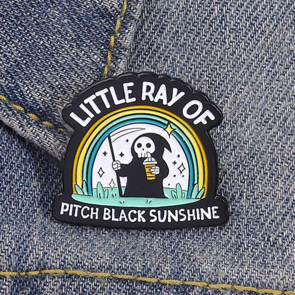 Emo Enamel pin with a design of a skeleton holding a coffee cup and rainbow, labeled 'Little Ray of Pitch Black Sunshine'.
