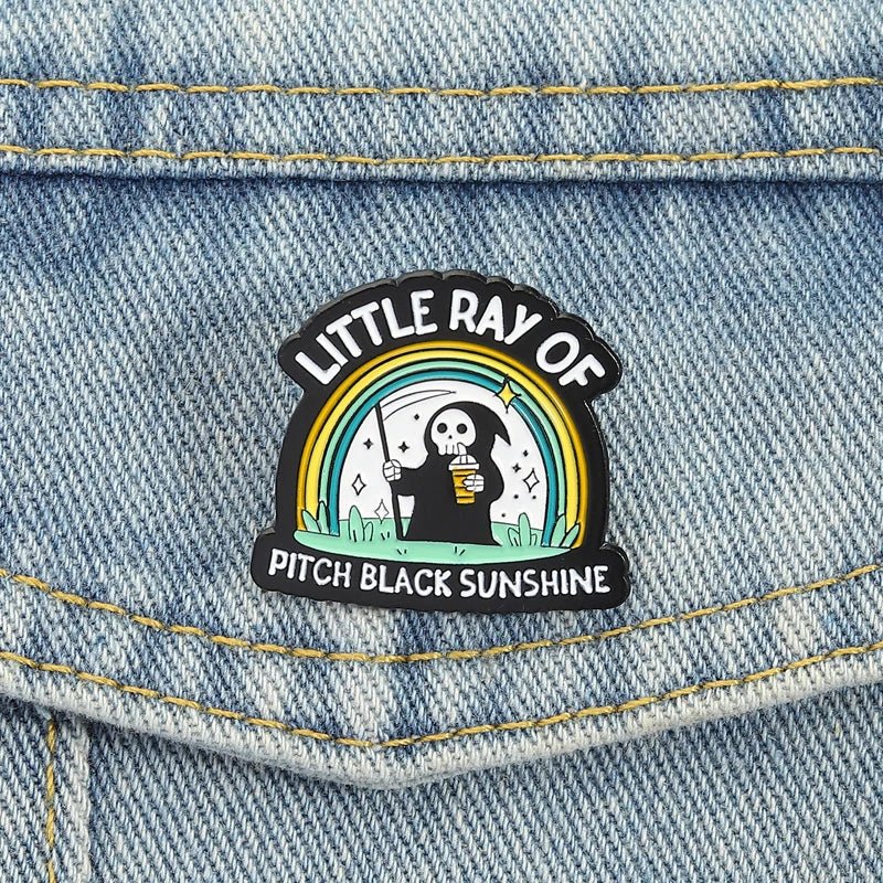Emo Enamel pin with a design of a skeleton holding a coffee cup and rainbow, labeled 'Little Ray of Pitch Black Sunshine'.