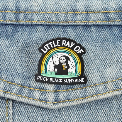Emo Enamel pin with a design of a skeleton holding a coffee cup and rainbow, labeled 'Little Ray of Pitch Black Sunshine'.